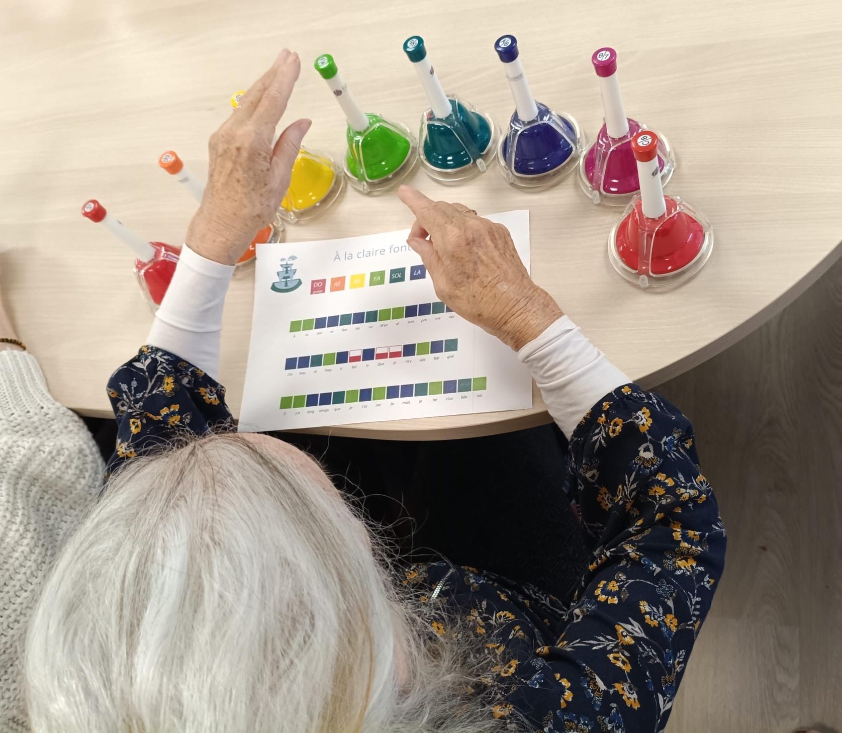 Une personne âgée fait une activité musicale avec des cloches colorées.
