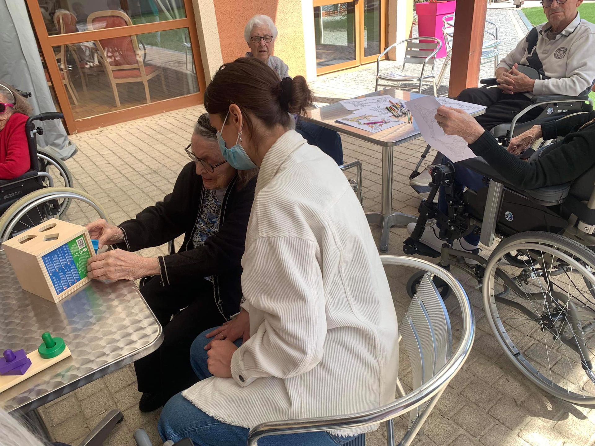 Une aide-soignante aide une personne âgée à effectuer une activité de tri de formes.