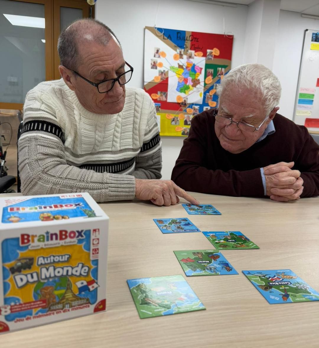 Deux personnes se penchent sur une table, étudiant des cartes de jeu colorées à côté d'une boîte BrainBox.