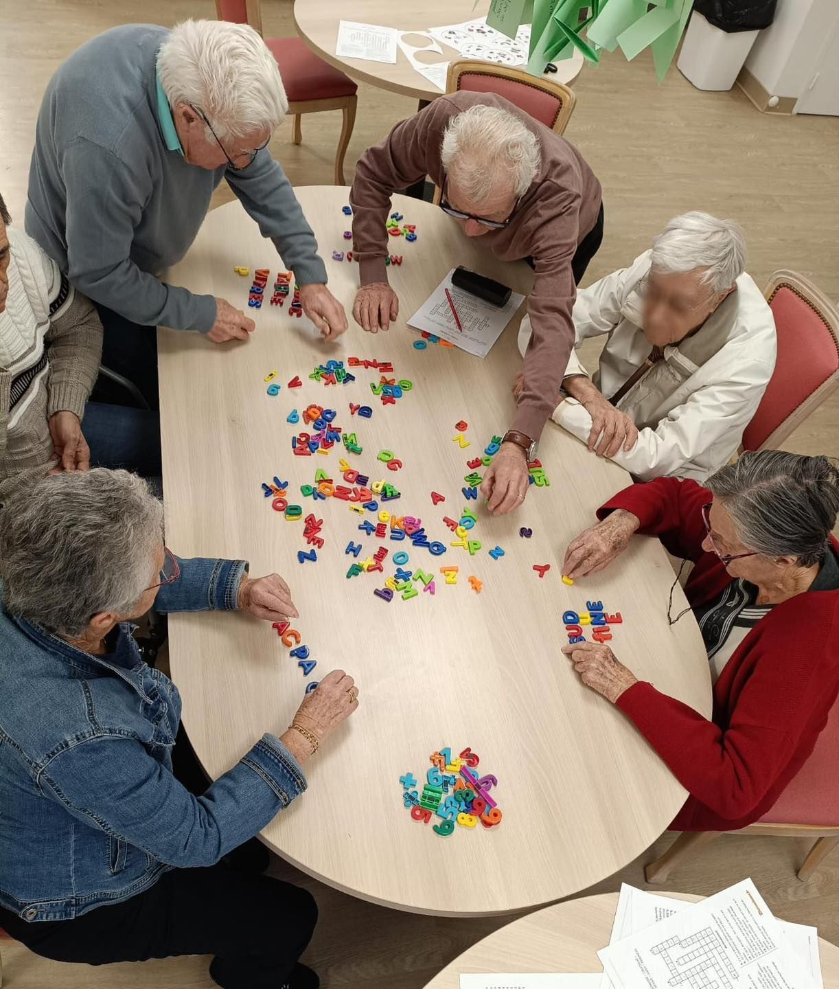 Un groupe de personnes âgées joue avec des lettres magnétiques colorées.