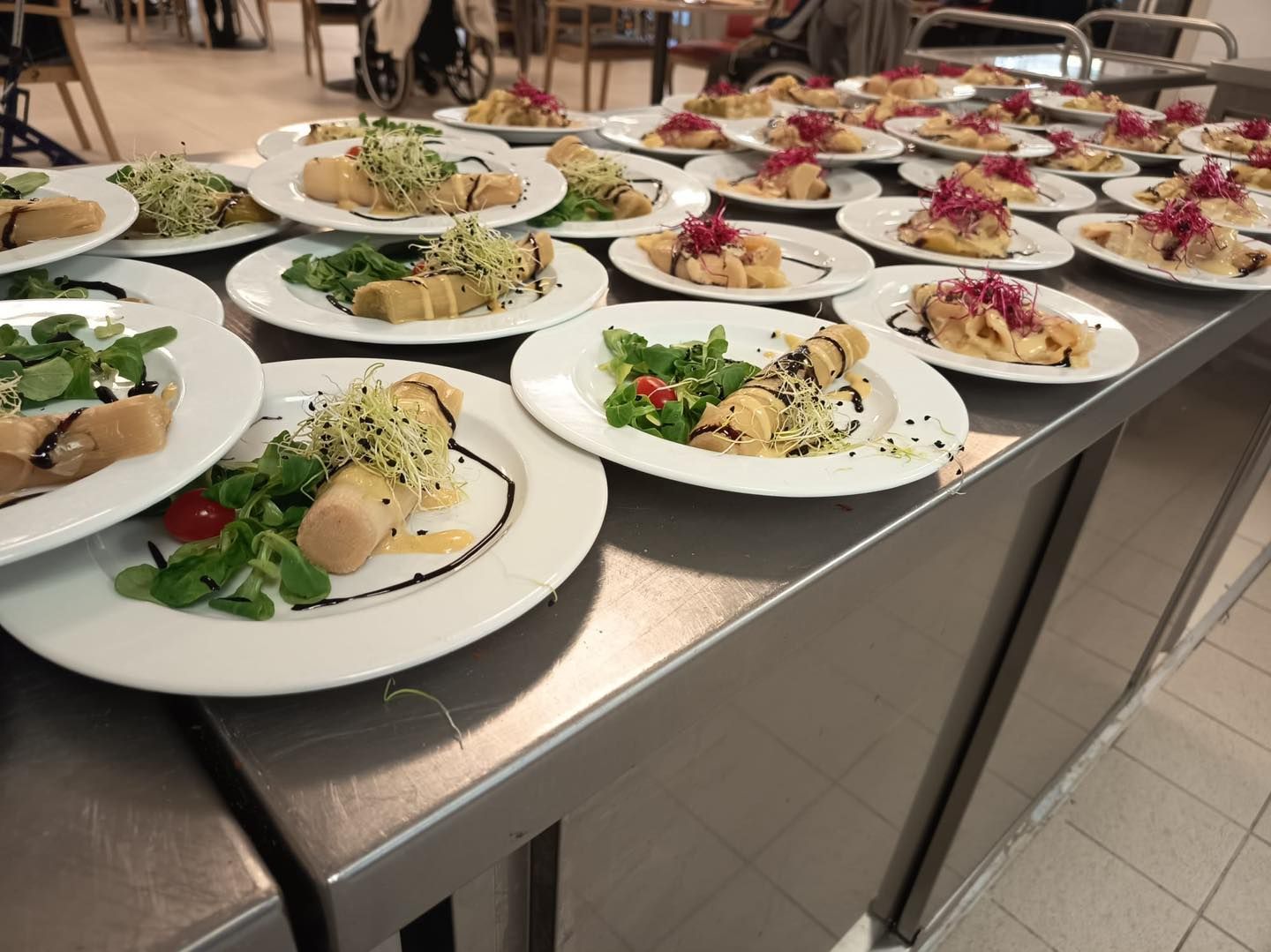 Assiettes de salades et d'amuse-bouches disposées sur des tables métalliques dans une cuisine.