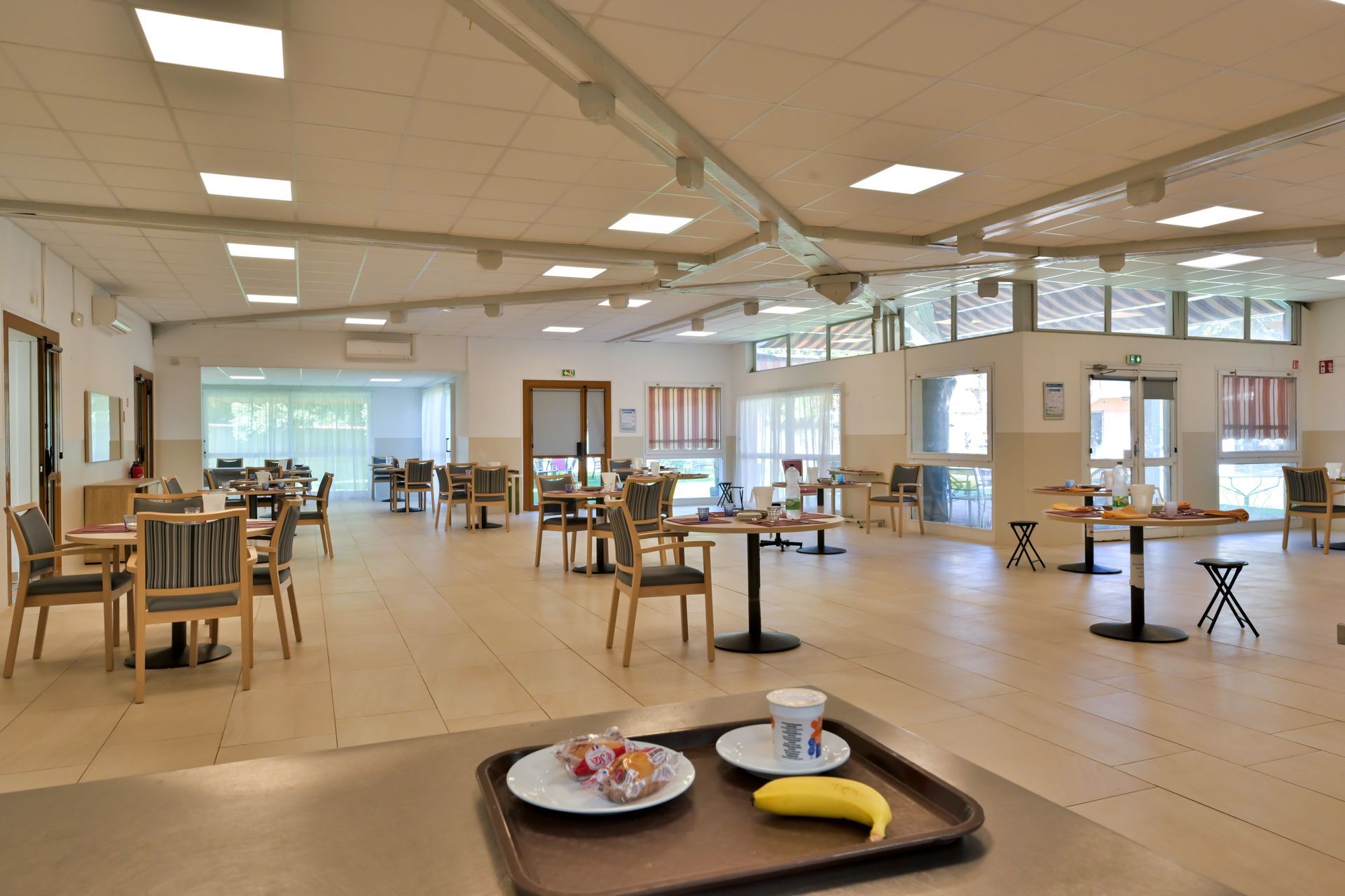 Un plateau avec une banane et de la nourriture est posé au premier plan d'une salle à manger lumineuse et spacieuse.