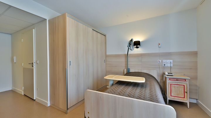 Une chambre d'EHPAD avec un lit, une armoire et une table de chevet.