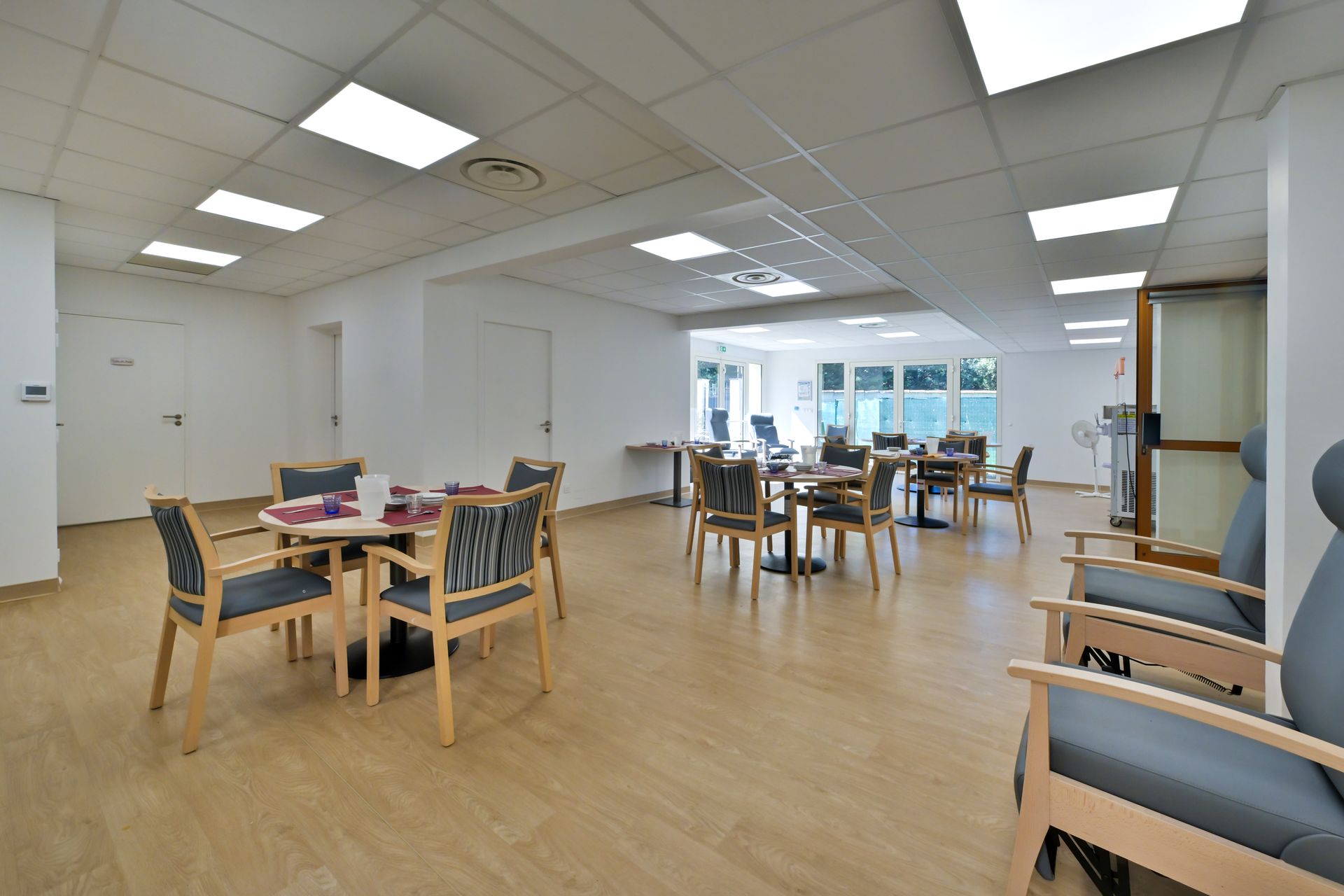 Une salle à manger moderne et lumineuse, avec des tables rondes, des chaises et un parquet clair à motifs.