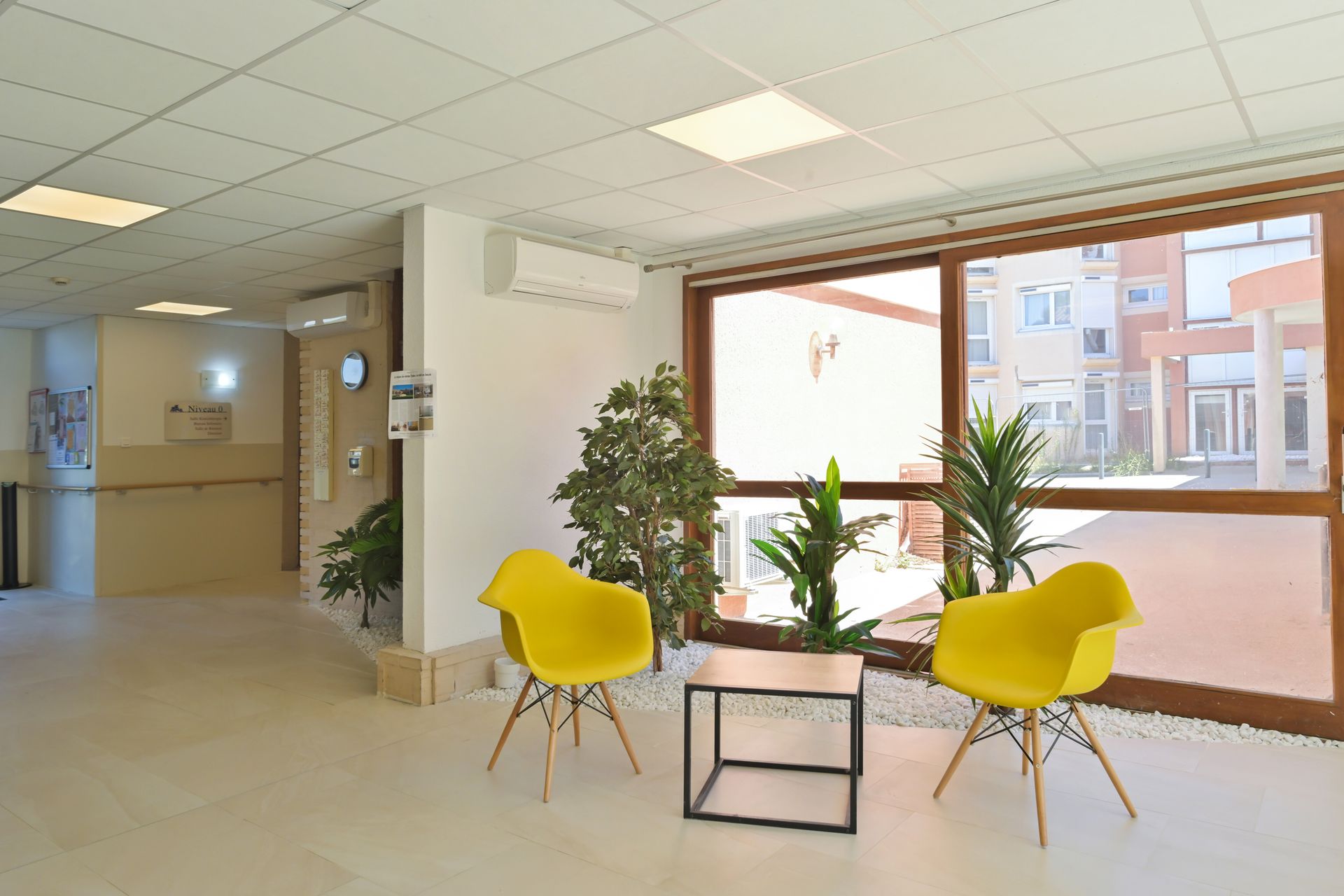 Une salle d'attente moderne avec deux chaises jaunes et une petite table entre elles.