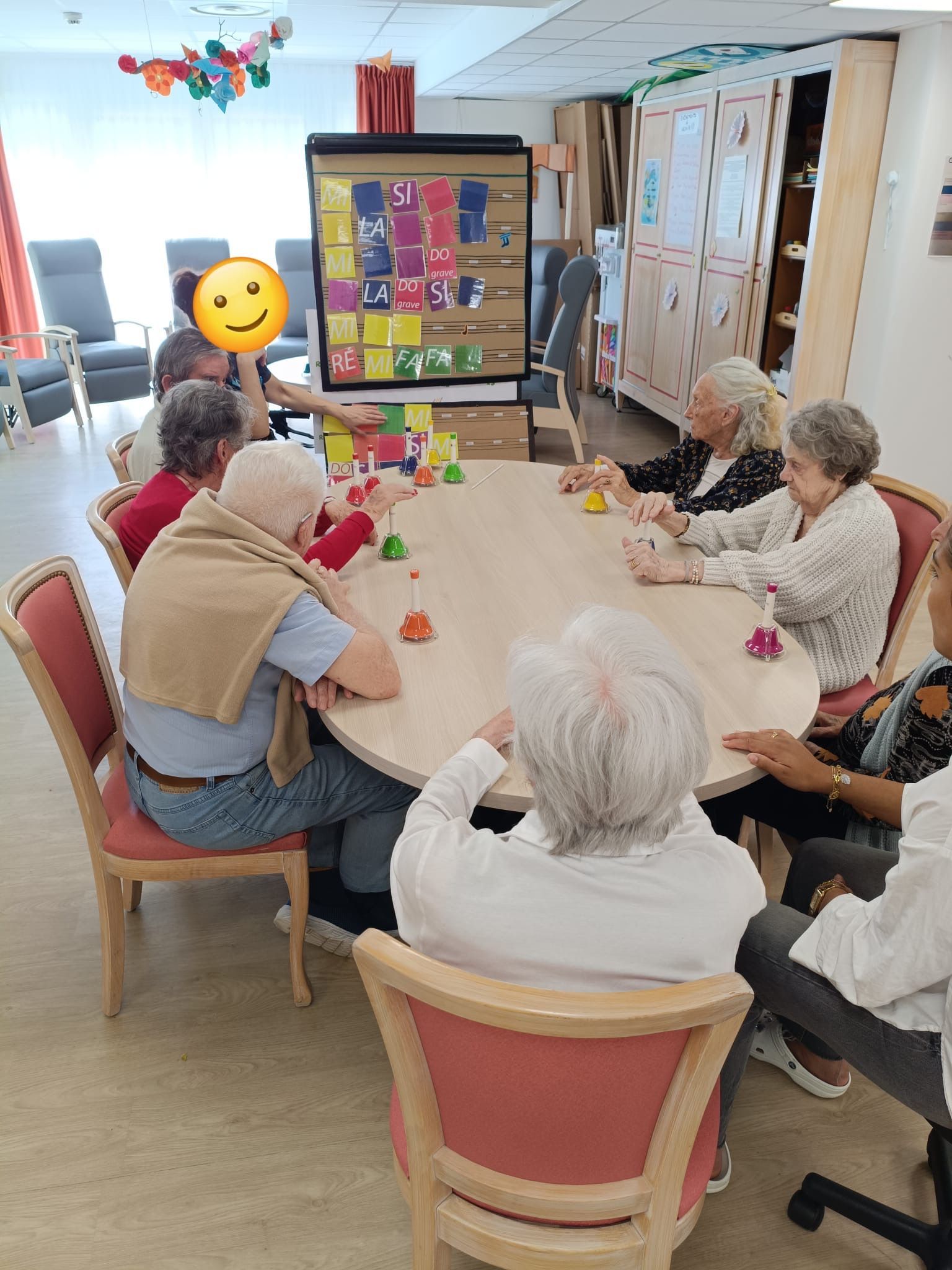 Des personnes assises autour d'une table jouent à un jeu de société dans une salle commune lumineuse.