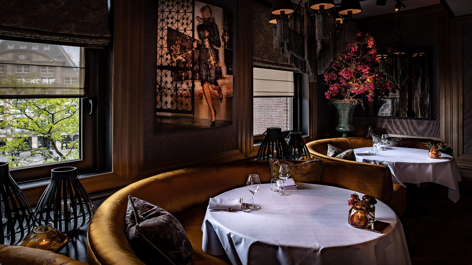 Eetgedeelte van een restaurant Bougainville met ronde tafels, gebogen gouden banken, grote ramen, kunstwerken.