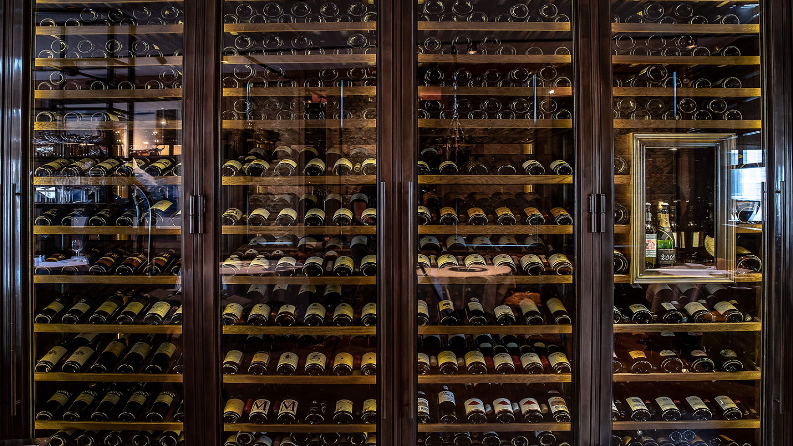 Houten wijnkast van restaurant Bougainville gevuld met verschillende flessen, met een spiegel aan de zijkant.