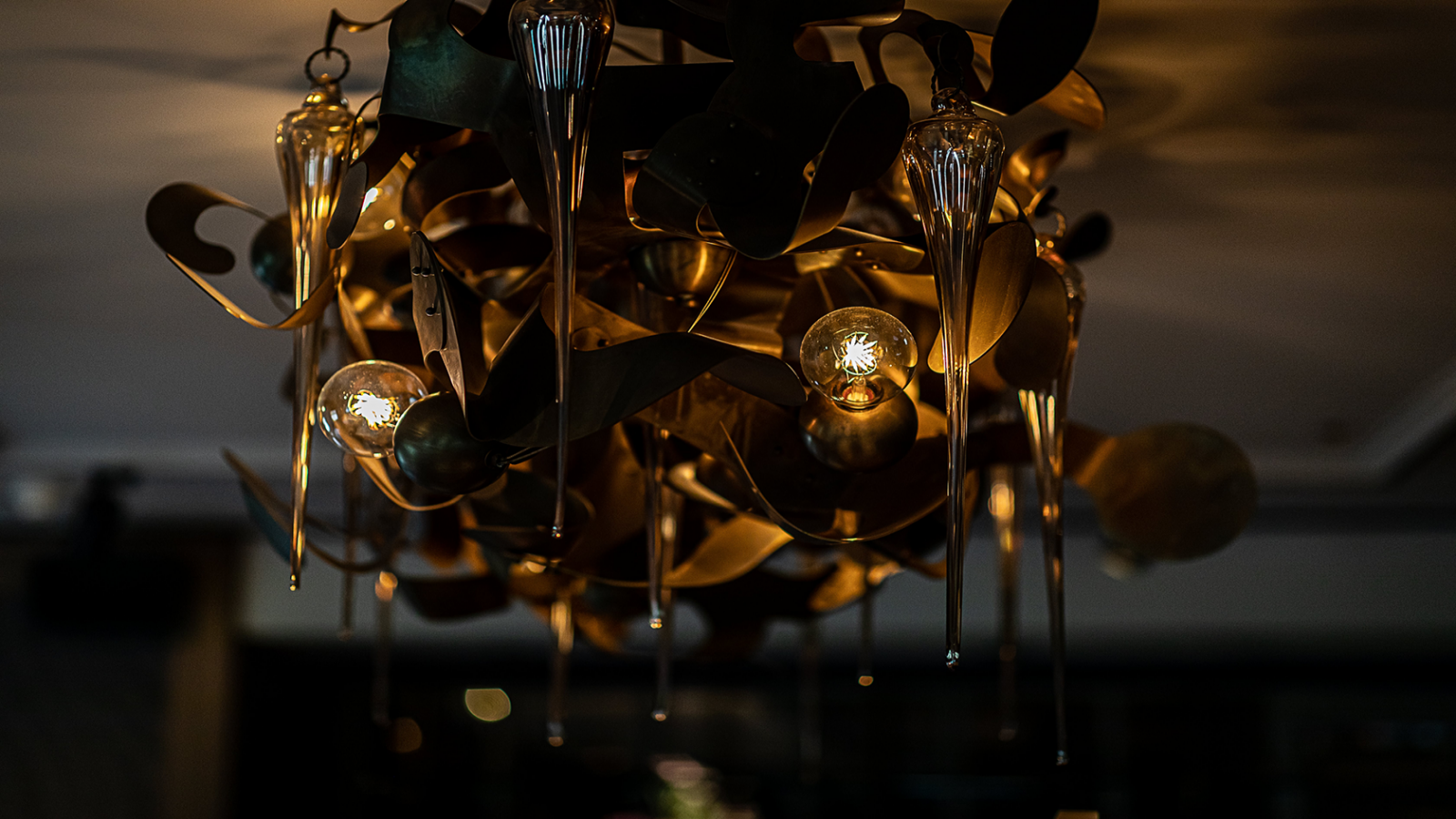 Versierde, donkerkleurige kroonluchter met gouden en decoratieve glasdruppels, hangend aan het plafond.