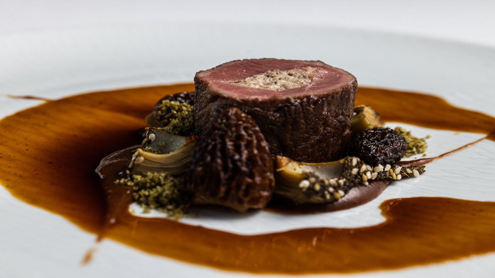 restaurant Bougainville: Een bord met een geroosterde vleesrol, omgeven door saus, champignons en kruiden.