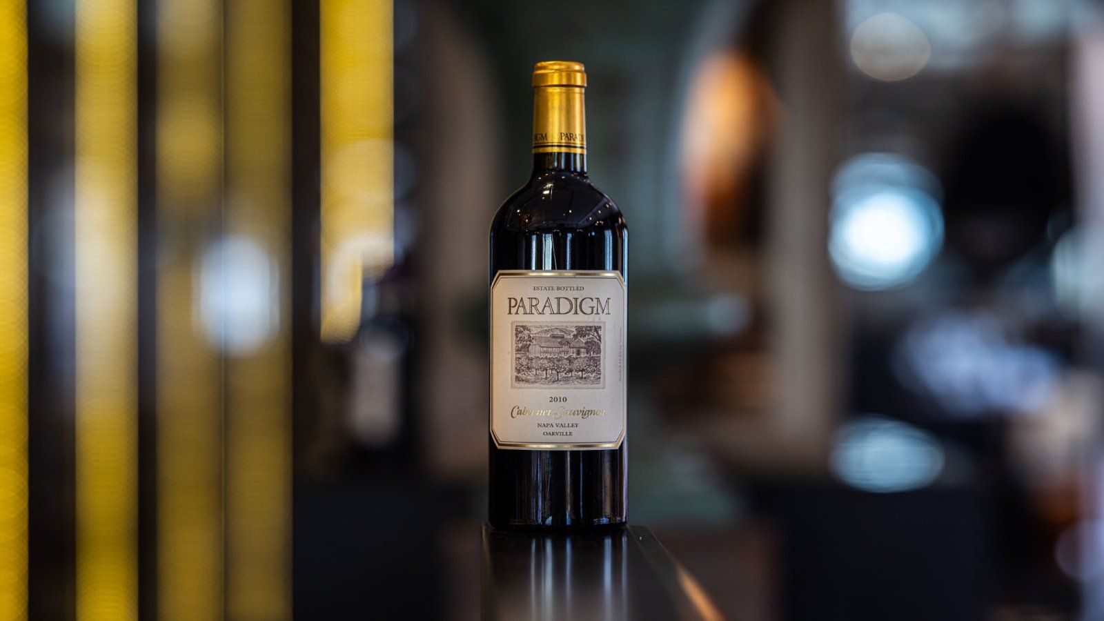 Fles rode wijn met gouden dop en etiket met QR-code, op een zwarte ondergrond.