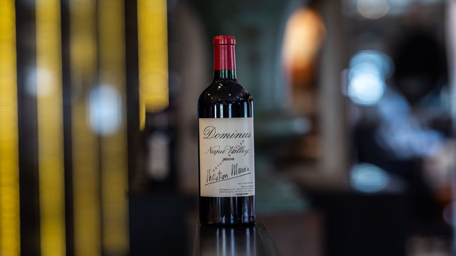 Een fles rode wijn met een handgeschreven etiket, tegen een onscherpe achtergrond.