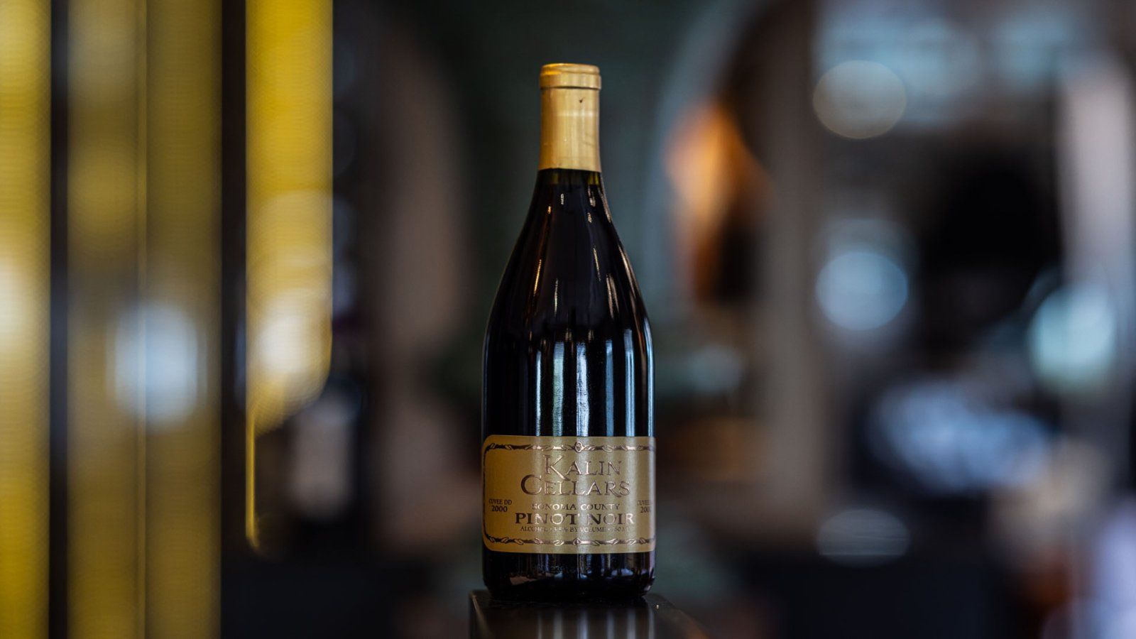 Wijnfles met goudfolie, donkere vloeistof, onscherpe achtergrond.