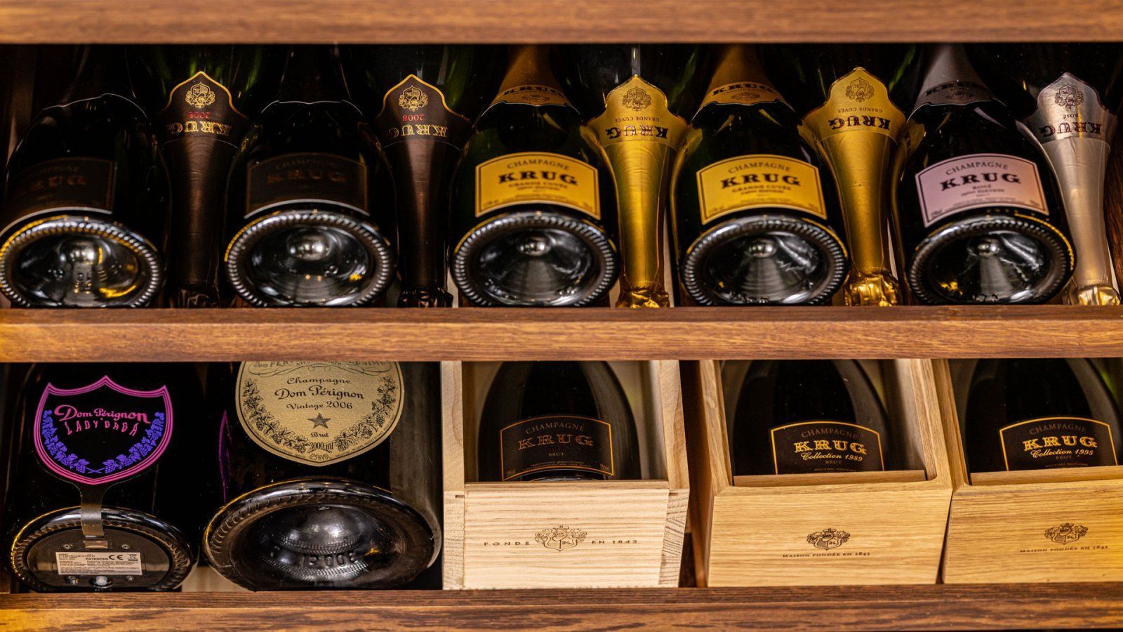 Wijnflessen in een houten rek: verschillende merken en kleuren champagne; sommige in dozen.