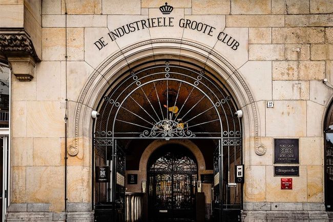 Entrance to "De Industriële Groote Club and Hotel TwentySeven" with arched doorway, iron gate, and sign.