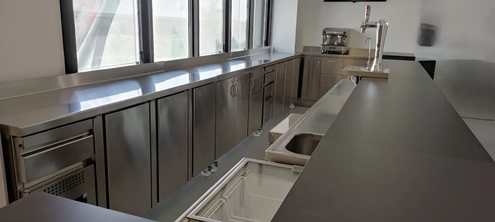 Barra de acero inoxidable con grifo y fregadero, y mostrador largo.