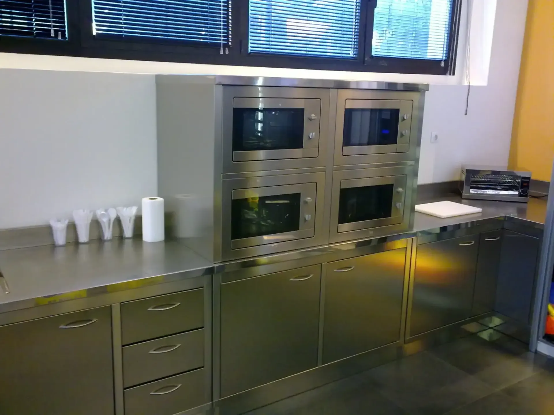 Gabinetes y encimeras de acero inoxidable en una habitación, con una ventana y tazas en el mostrador.