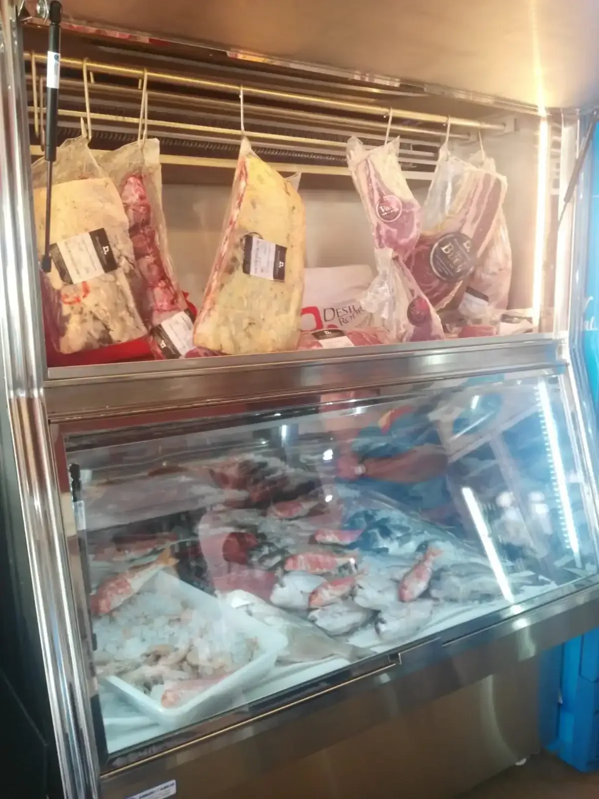 Vitrina expositora de carnes y pescados con cortes envasados colgantes y artículos frescos expuestos.