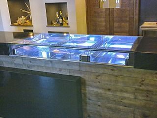 Bar comercial con vitrina de cristal con iluminación azul, insertado en una estructura de madera y piedra.