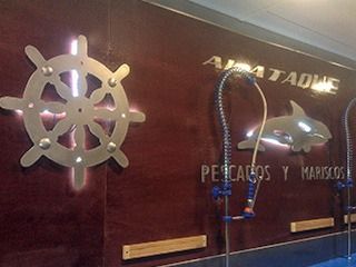 Timón de barco y emblema de orca en la pared de un restaurante, anunciando mariscos.