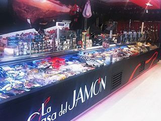 Vitrina refrigerada rotulada “La Casa del Jamon” con diversos embutidos.