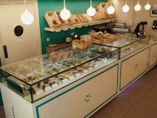 Vitrina de panadería con pasteles y productos horneados. Interior blanco y verde azulado, con iluminación cenital.