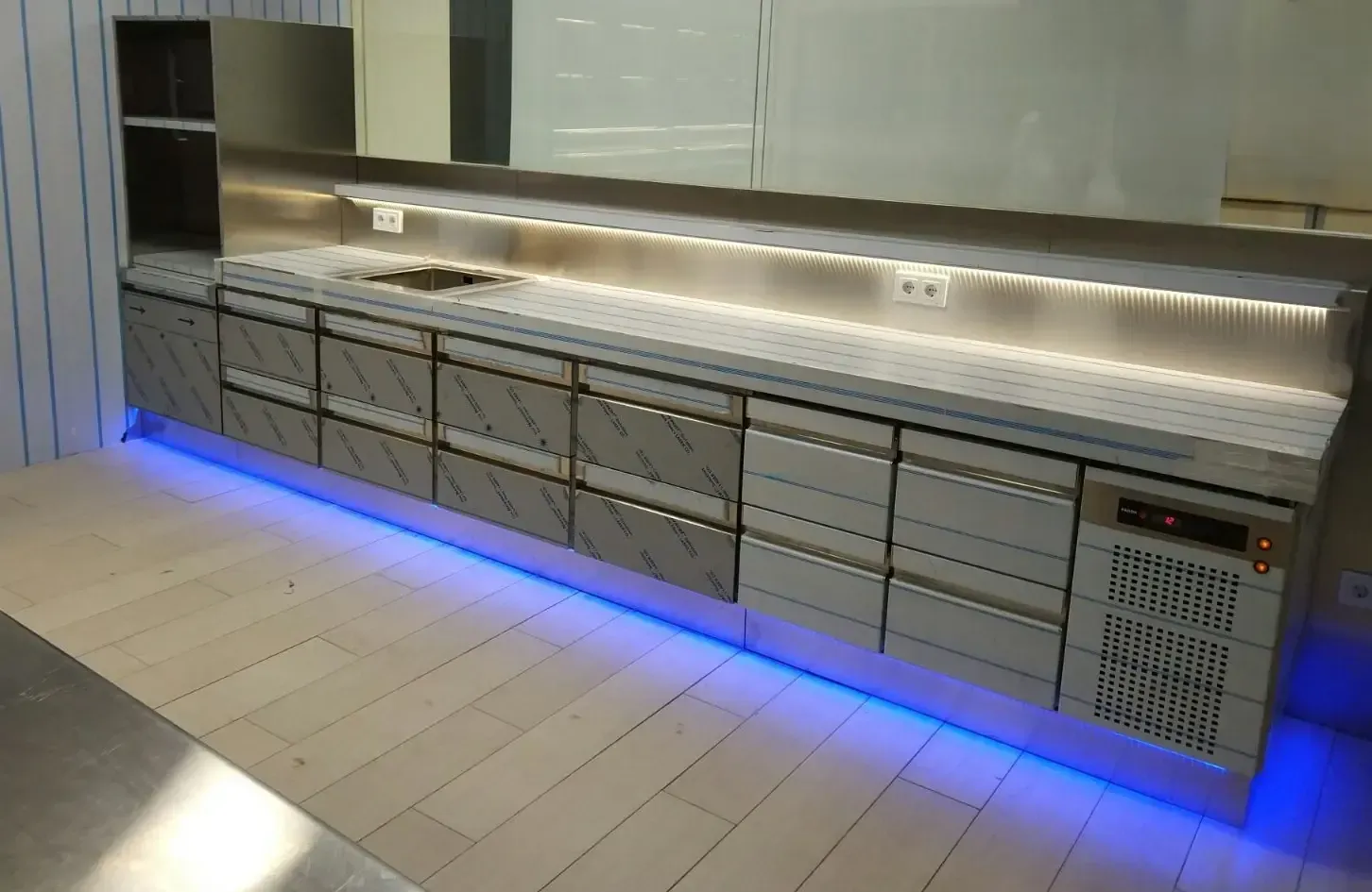 Mostrador de cocina comercial de acero inoxidable con cajones, luces y unidad frigorífica.