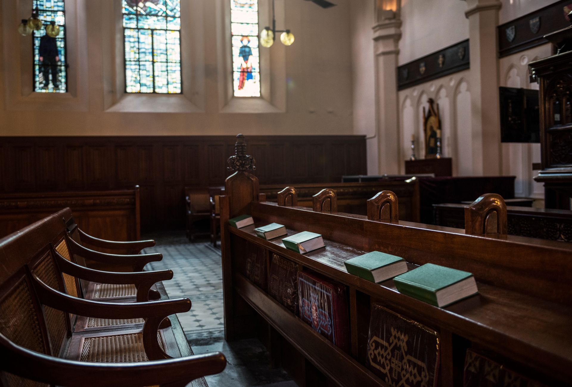 Interior de uma igreja com bancos de madeira, vitrais e livros.