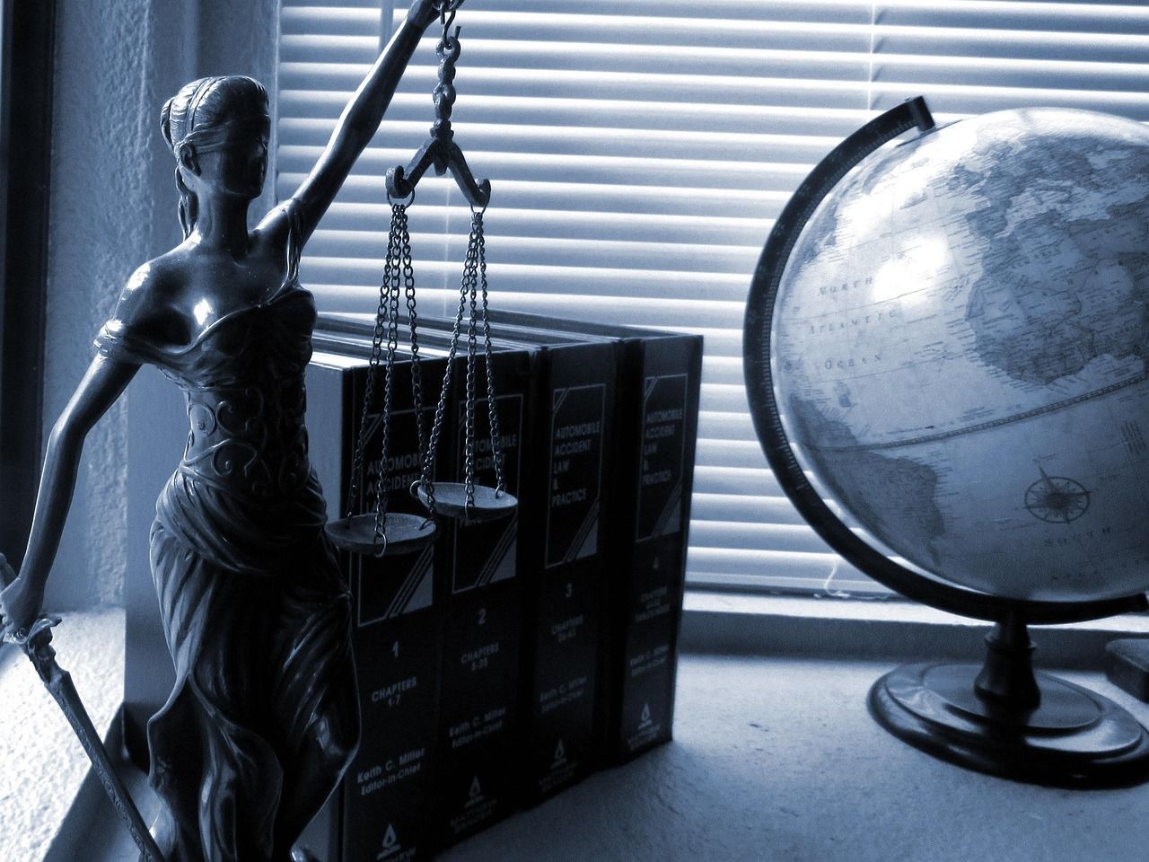 Estátua da Senhora Justiça com balança e espada, livros de leis, globo e janela com persianas.