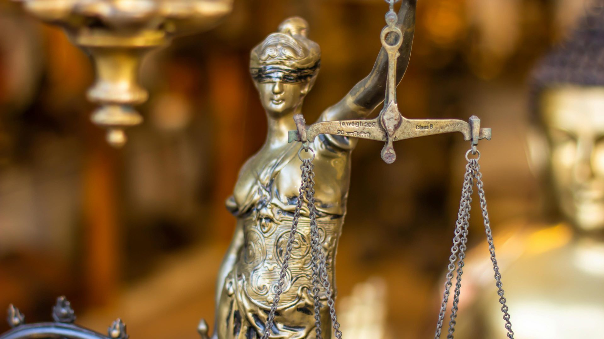 Estátua dourada da Senhora Justiça segurando uma balança, com os olhos cobertos, em uma vitrine.