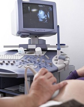 Máquina de ultrasonido que escanea el abdomen de una persona y muestra imágenes en la pantalla.