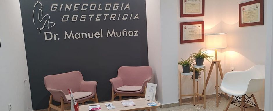 Interior de un consultorio médico con sala de espera. Presenta una pared negra con acentos de texto blanco y dos sillones rosas.