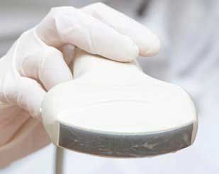 Mano con transductor de ultrasonido. Guante blanco, dispositivo curvo con superficie gris oscura.