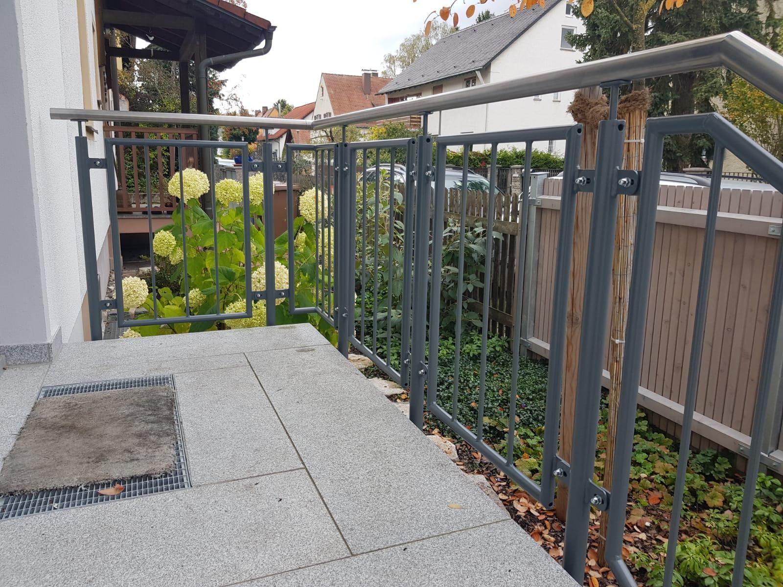 Außenrampe mit Metallhandlauf entlang eines gefliesten Gehwegs neben einer weißen Mauer und Bäumen