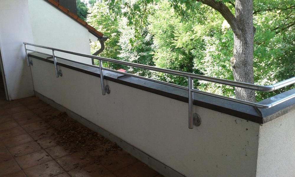 Außenrampe mit grauem Geländer und Betonfläche neben einem Haus und einem Gartenzaun