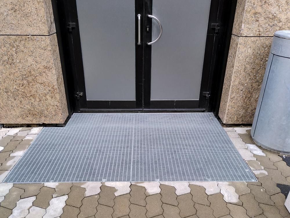 Außenrampe mit Metallhandlauf entlang eines gefliesten Gehwegs neben einer weißen Mauer und Bäumen