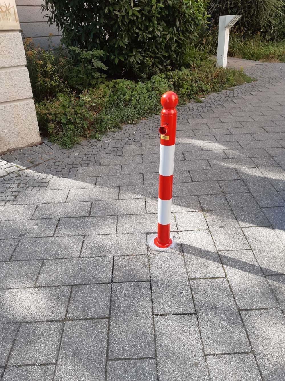 Außenrampe mit Metallhandlauf entlang eines gefliesten Gehwegs neben einer weißen Mauer und Bäumen