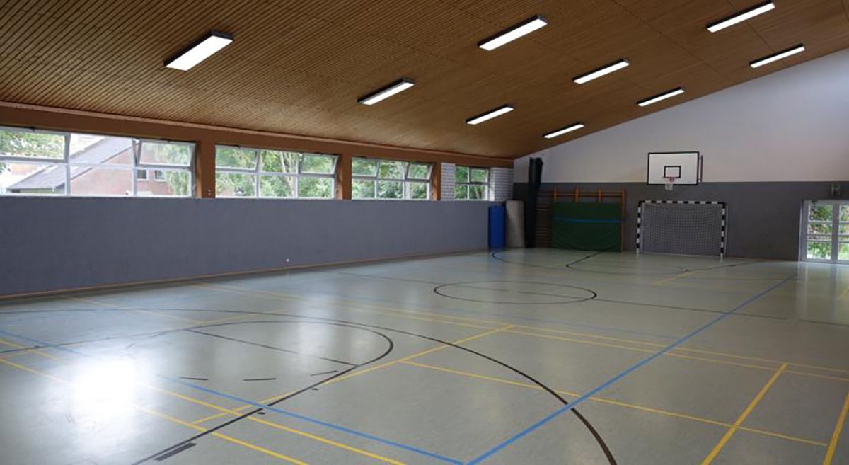 Leere Turnhalle mit Holzdecke, Basketballkorb und großen Fenstern entlang der Wand