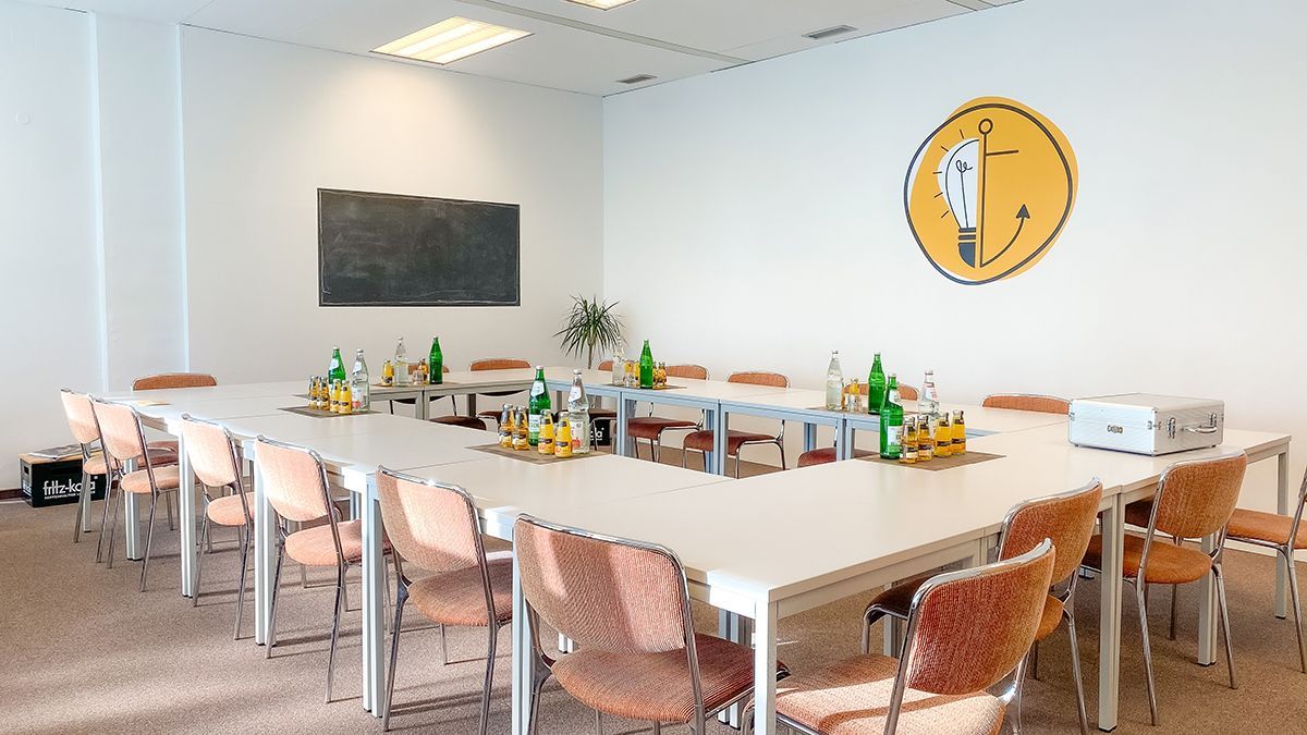 Heller Konferenzraum mit einem langen Tisch, gedeckt mit Getränken, Gläsern und Stühlen, vor weißen Wänden