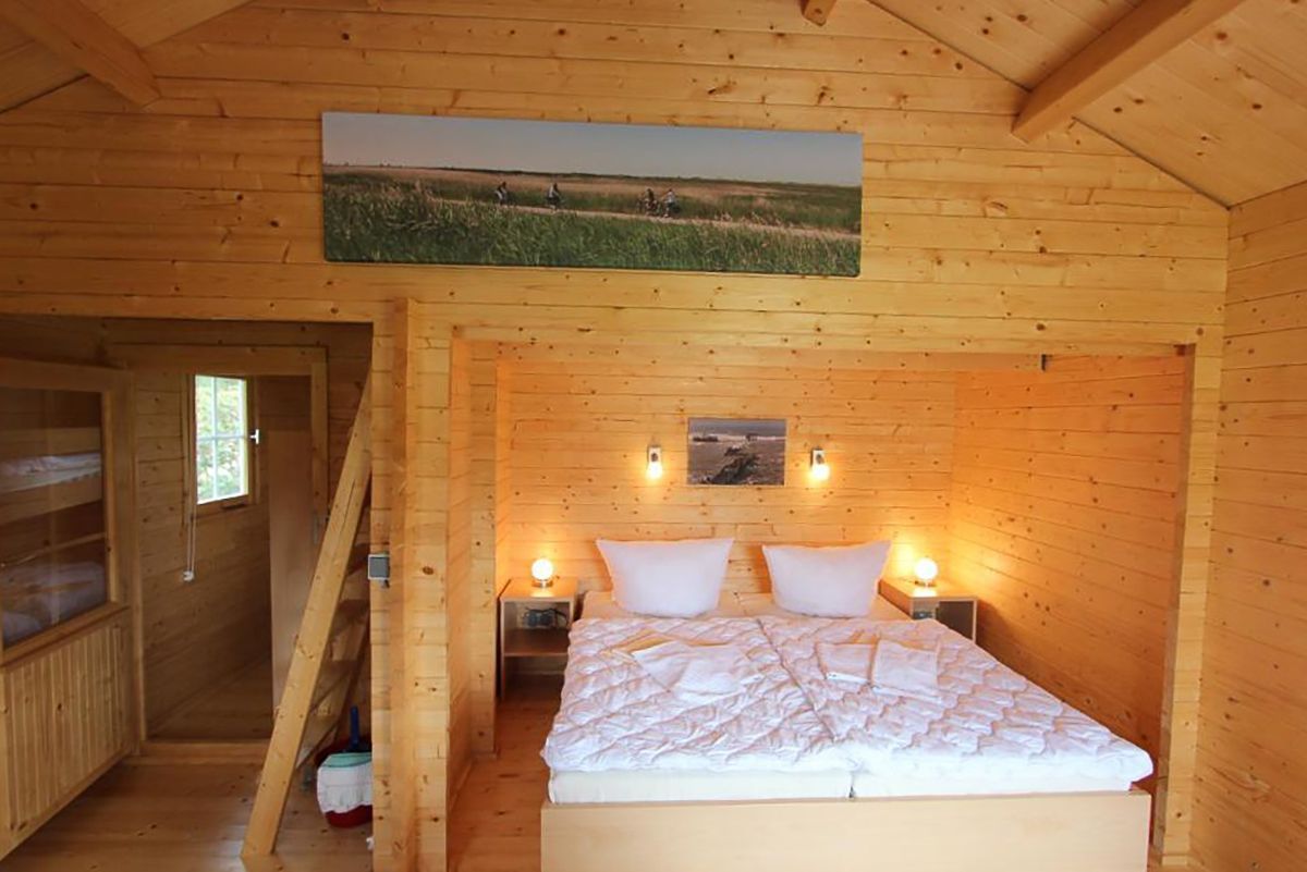 Gemütliches Schlafzimmer aus Holz mit Doppelbett, warmen Lampen und Landschaftsbildern an der Wand.
