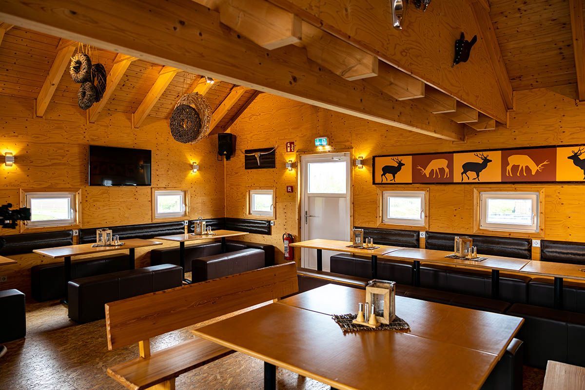 Gemütlicher Speisesaal im Landhausstil mit Holzbalken, Tischen, Sitznischen und an der Wand montierten Fernsehern