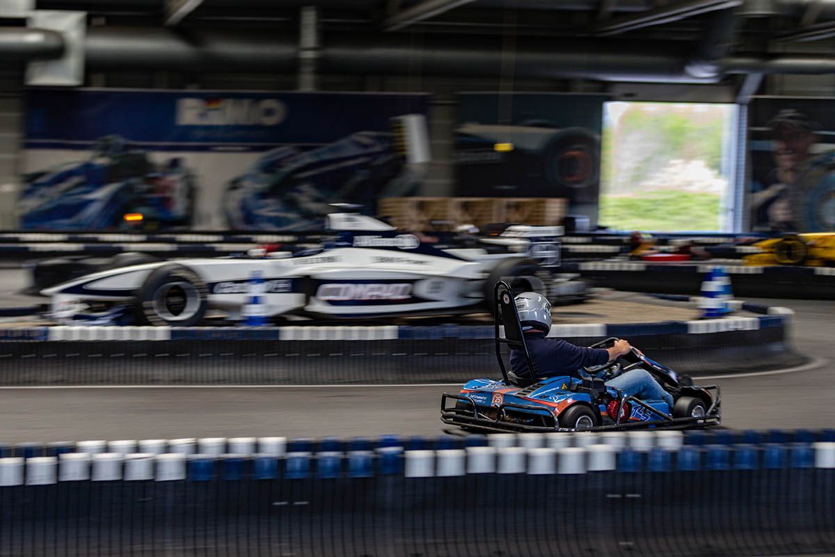 Go-Karts rasen auf einer Indoor-Bahn, im Vordergrund ein blau-schwarzes Kart, die anderen sind dahinter verschwommen zu sehen.