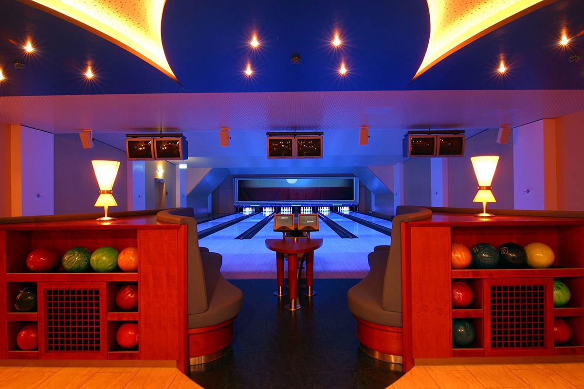 Eine neonbeleuchtete Bowlingbahn mit roten Sitzen, Bowlingkugeln und Bahnen, die zu leuchtenden Kegeln führen.