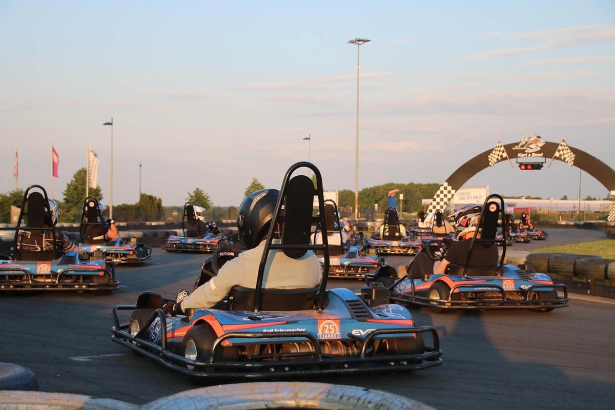 Go-Karts rasen bei Sonnenuntergang auf einer Rennstrecke; im Hintergrund sind ein Torbogen und Lichter zu sehen.