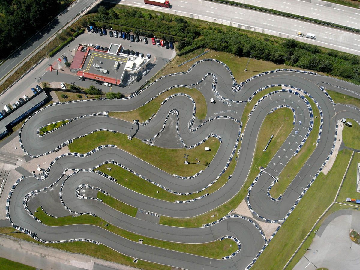 Luftaufnahme einer kurvenreichen Go-Kart-Bahn, auf der viele Karts um die Kurven rasen.