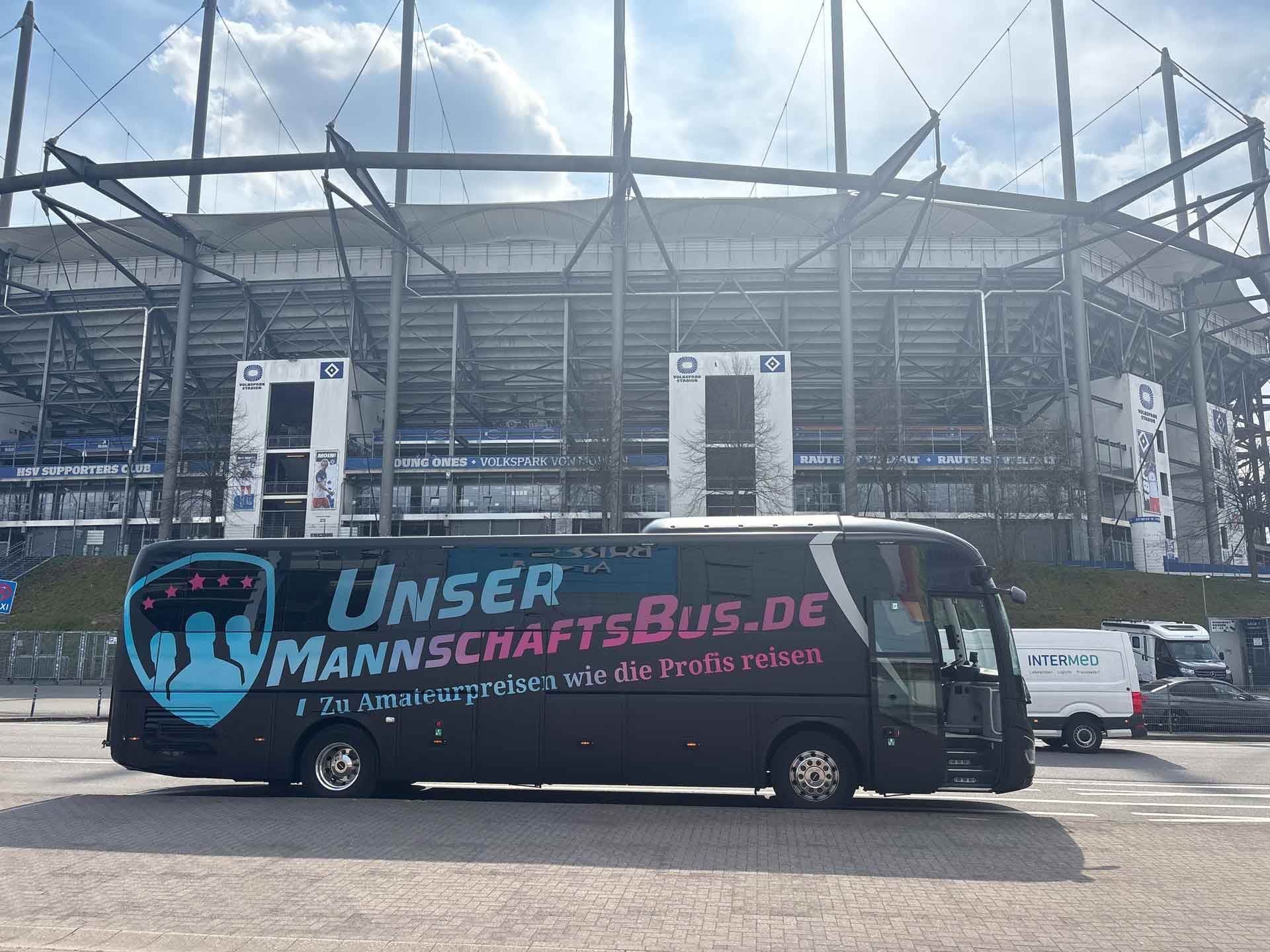 Ein großer schwarzer Fanbus mit der Aufschrift „UNSERMANSCHAFTFUS.DE“ an der Seite parkt vor einem Stadion.