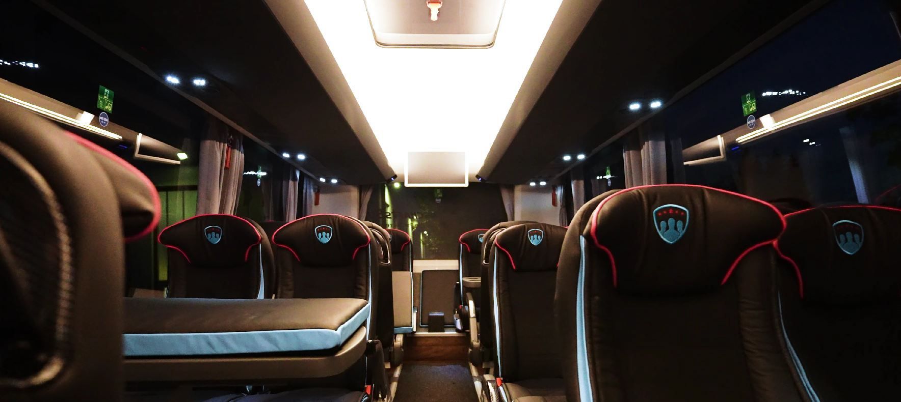 Leerer Innenraum eines Luxusbusses mit Reihen schwarzer Ledersitze und Deckenbeleuchtung.