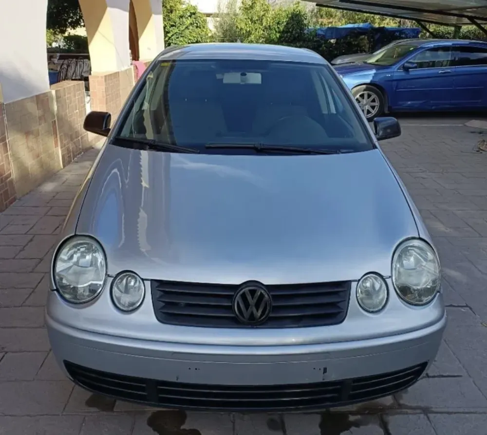 Vista frontal de un Volkswagen plateado aparcado al aire libre en una entrada pavimentada con baldosas.