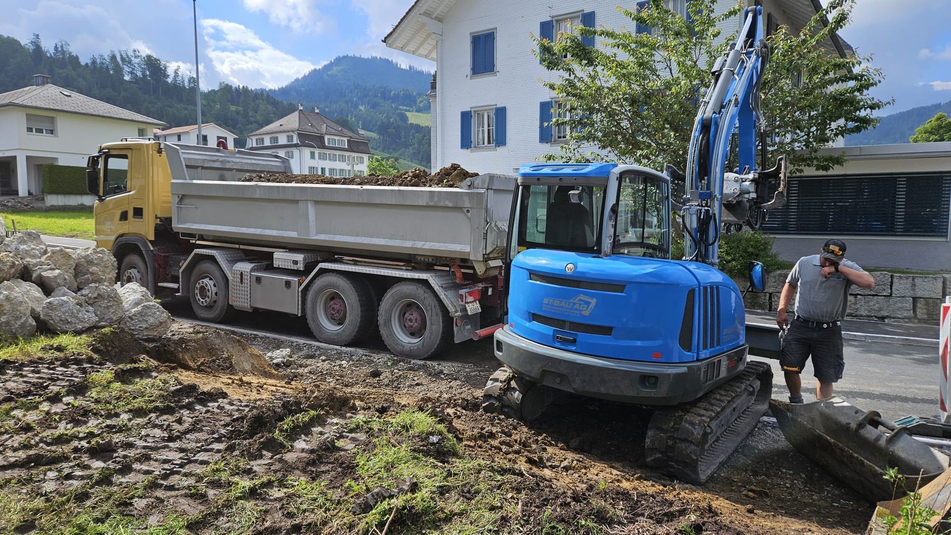 Ein Mann steht neben einem Muldenkipper und einem Bagger.