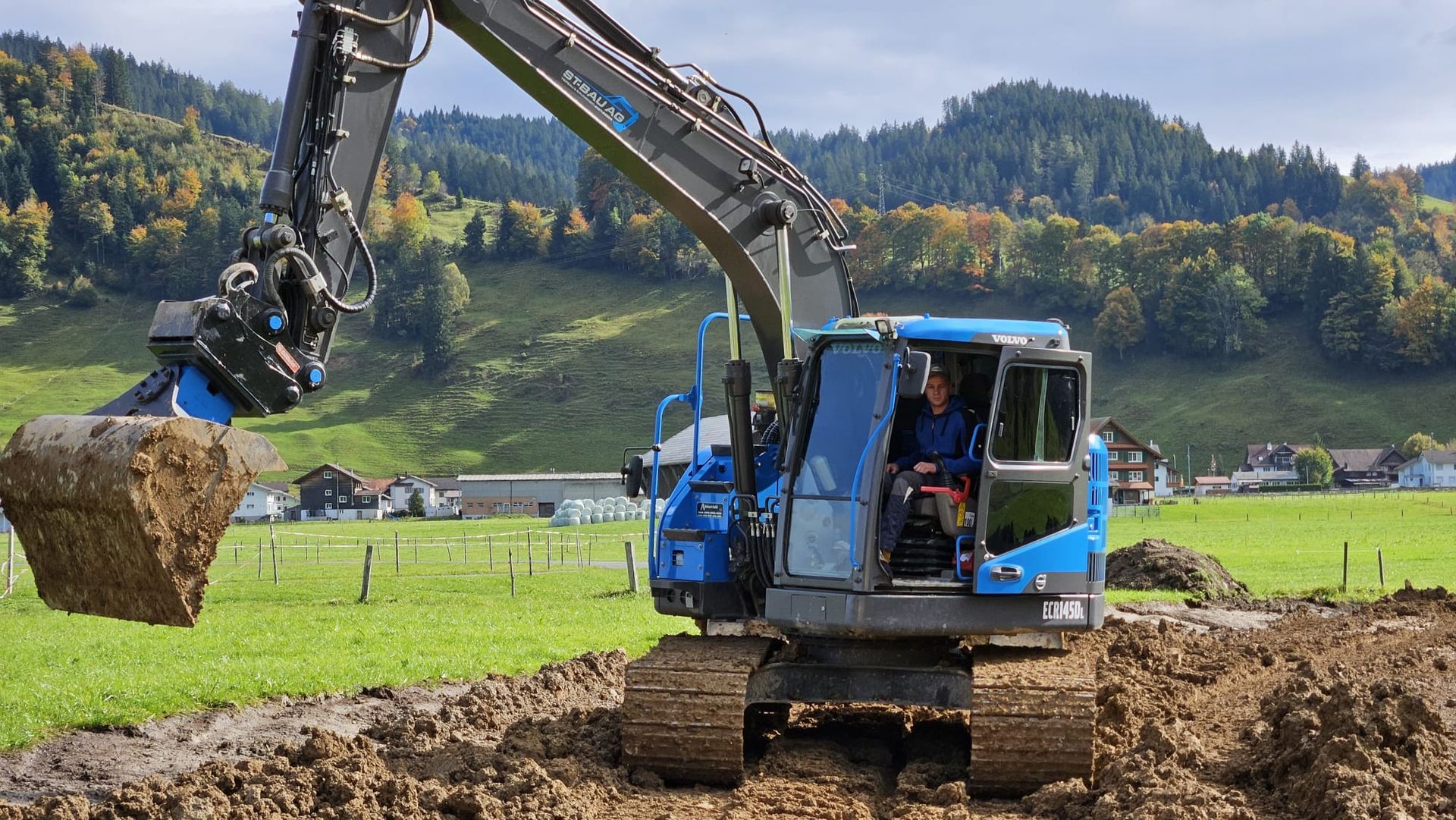 Ein Mann fährt einen blauen Bagger über ein Feld.